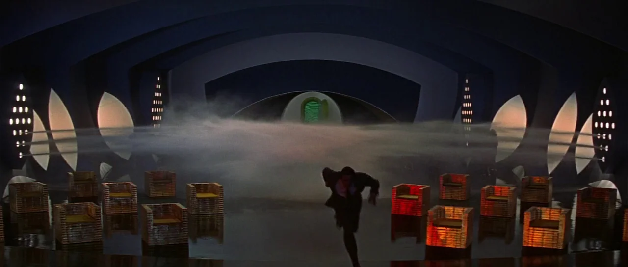 Casino Royale (1967) (1967) movie still: wide — A wide, dark futuristic space features glowing geometric seating and a central green portal. A man…