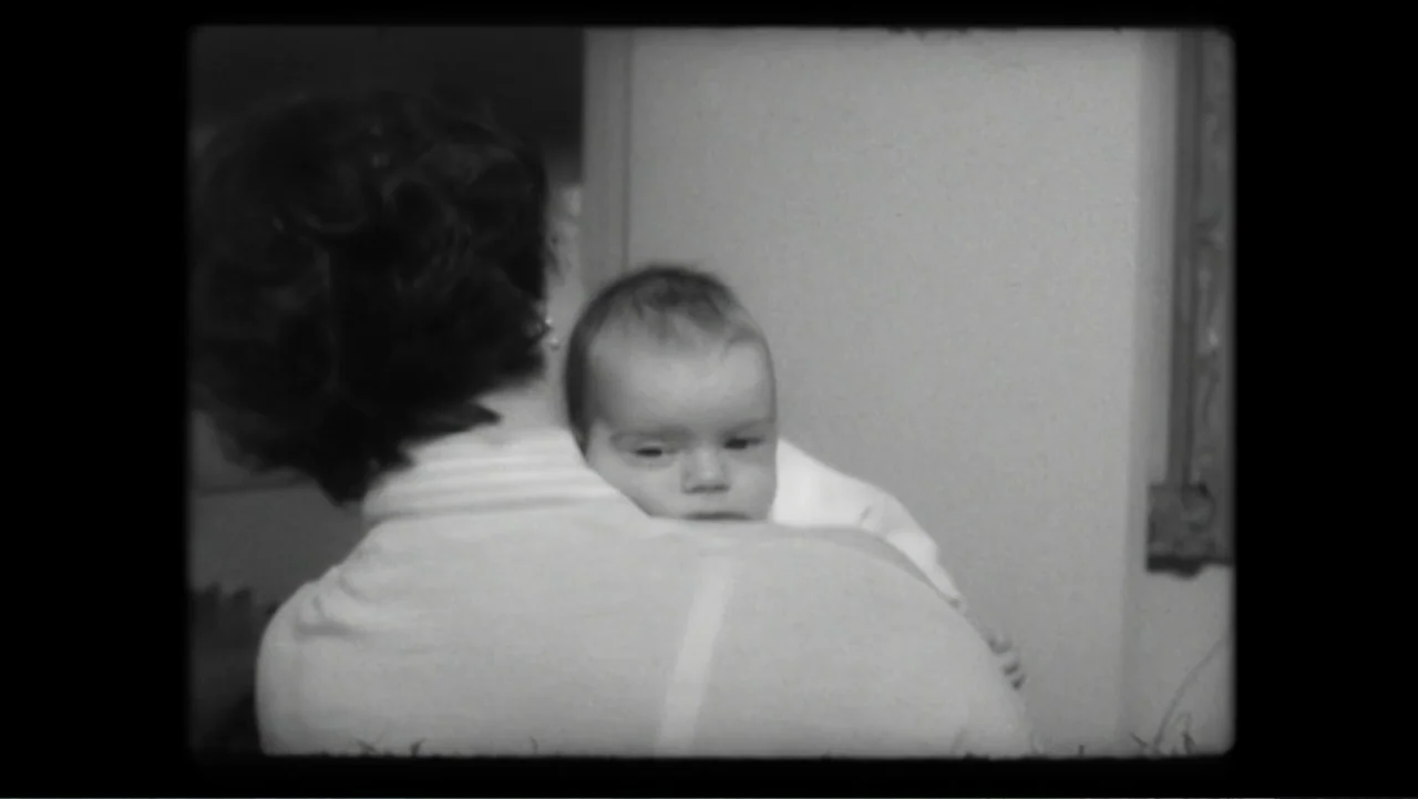 Elizabeth Taylor: The Lost Tapes (2024) movie still: medium — An interior space features a person carrying an infant. The adult holds the baby…