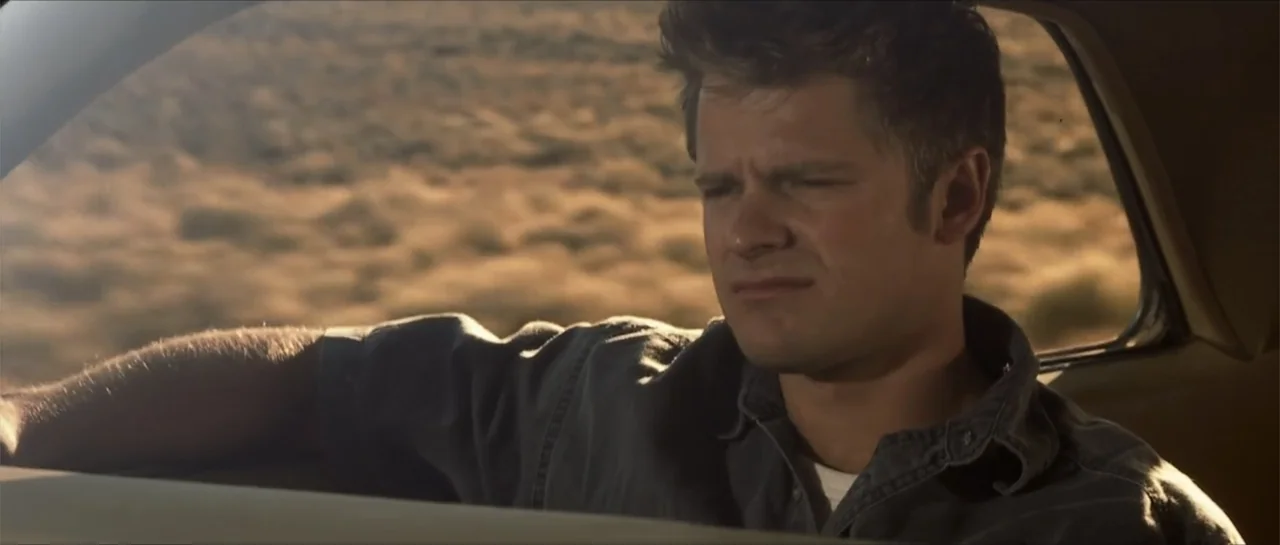 Joy Ride (2001) movie still: medium — A man sits inside a vehicle moving through an arid desert landscape at sunset. The subject looks out the…