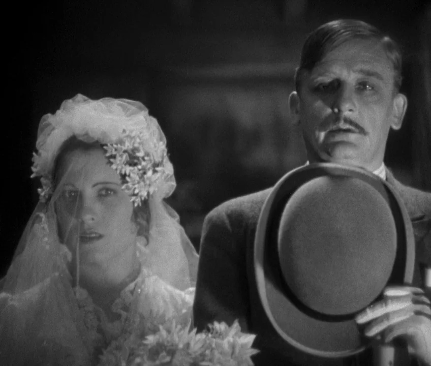 The Threepenny Opera (1931) movie still: medium — A man and woman stand together in a dark room during a wedding ceremony. The woman wears a veil…