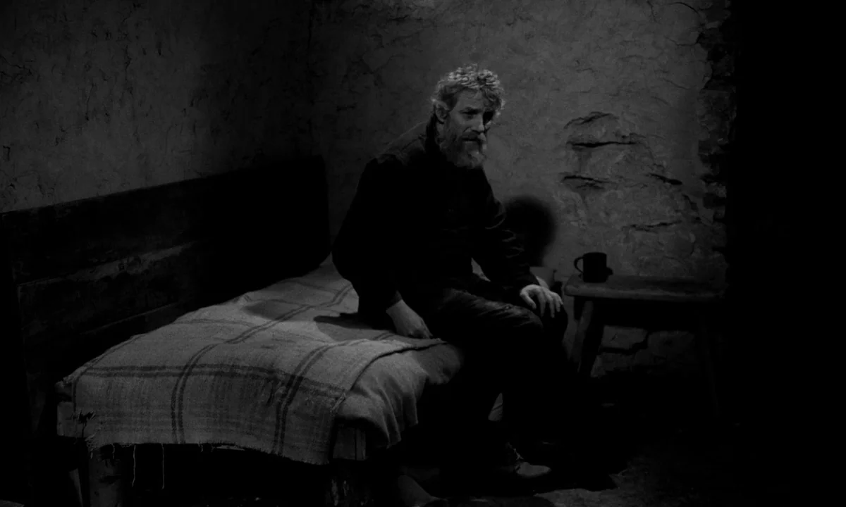 The Turin Horse (2011) movie still: medium — A austere stone-walled room features a simple wooden bed and a small side stool. A middle-aged bearded…
