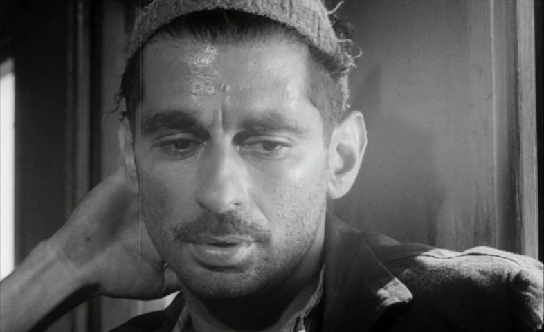 Cairo Station (1958) movie still: closeup — A dimly lit passenger train car features wooden interior walls and simple window frame. A man wearing a…