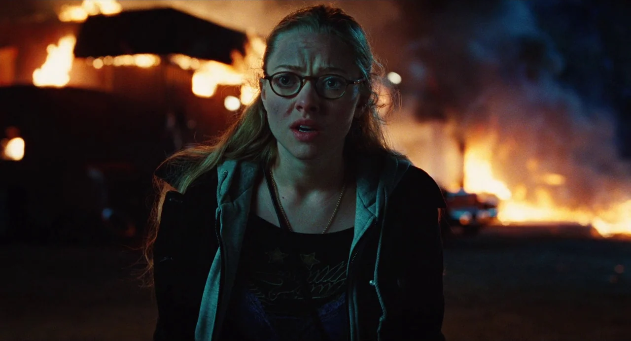 Jennifer’s Body (2009) movie still: medium — A dark night setting featuring an active, out-of-control fire in the background. A young woman stands…