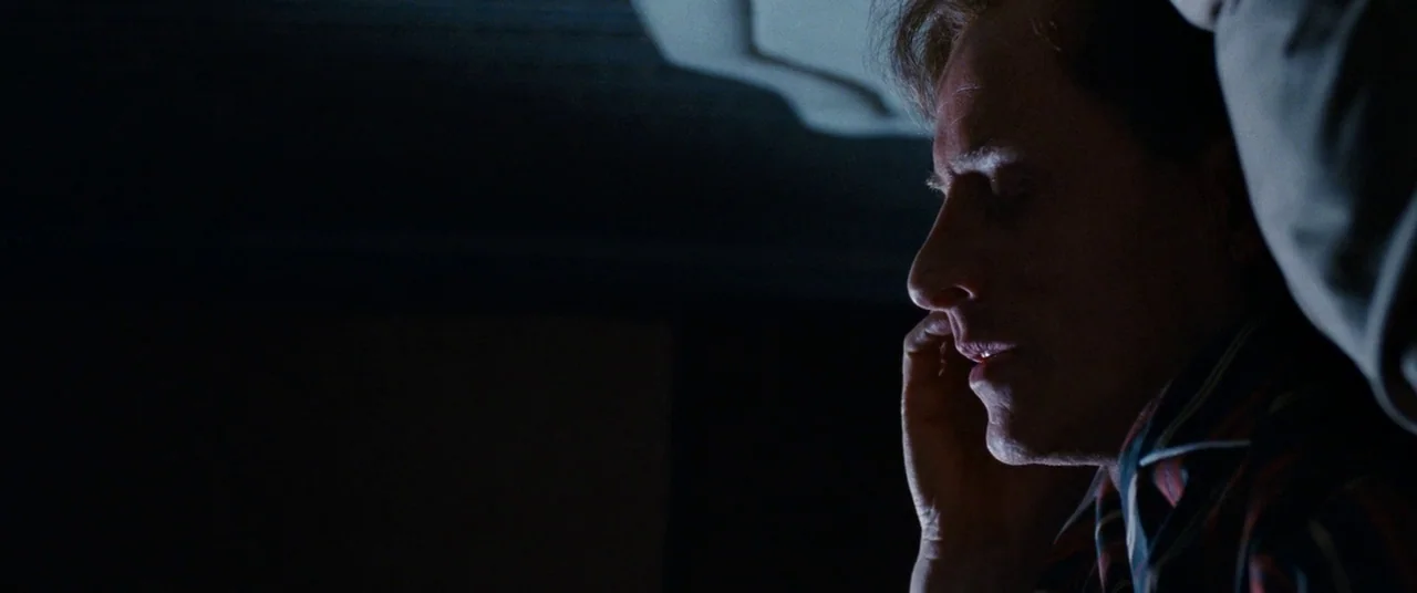 Cloud Atlas (2012) movie still: closeup — A dark, dimly lit bedroom at night with minimal architectural detail visible. A man lies in bed with his…