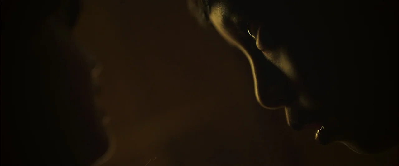 The Unholy (2022) movie still: closeup — A dark indoor space with minimal ambient light. Two individuals stand face to face in a very tight space.
