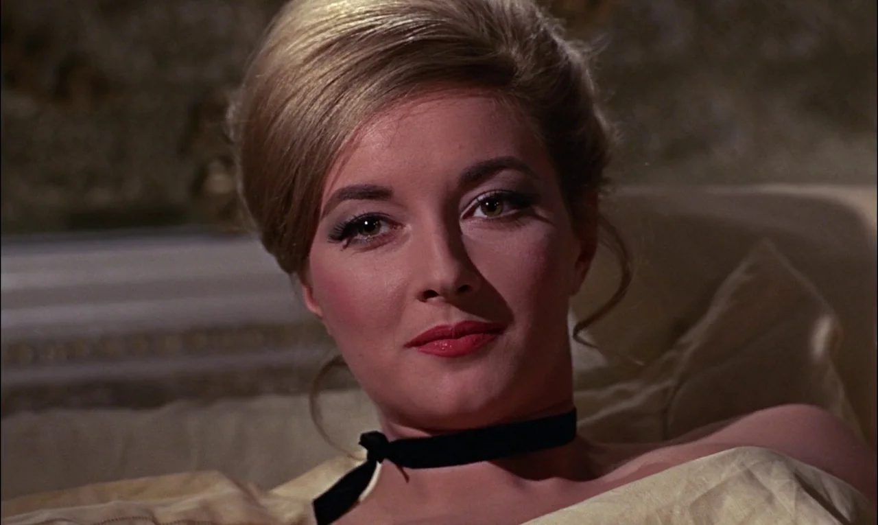 From Russia With Love (1963) movie still: closeup — A woman rests on a bed inside a dimly lit room with ornate wallpaper. She looks directly toward…