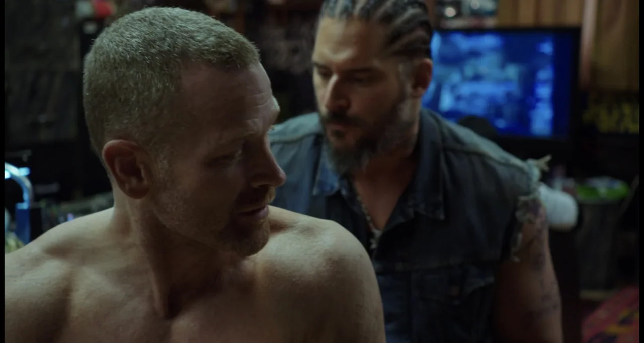 Sabotage (2014) movie still: medium — An interior studio space featuring dark textures and a glowing computer monitor background. A man with braided…