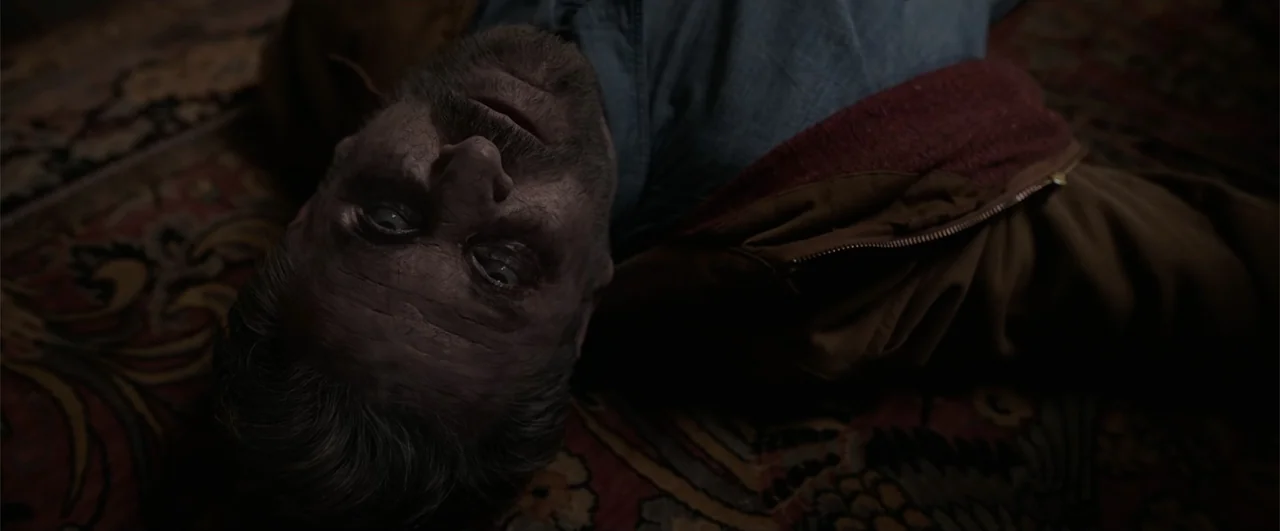 Annabelle: Creation (2017) movie still: closeup — A man lies on his back on a patterned textile surface. The man stares upward with wide, discolored…
