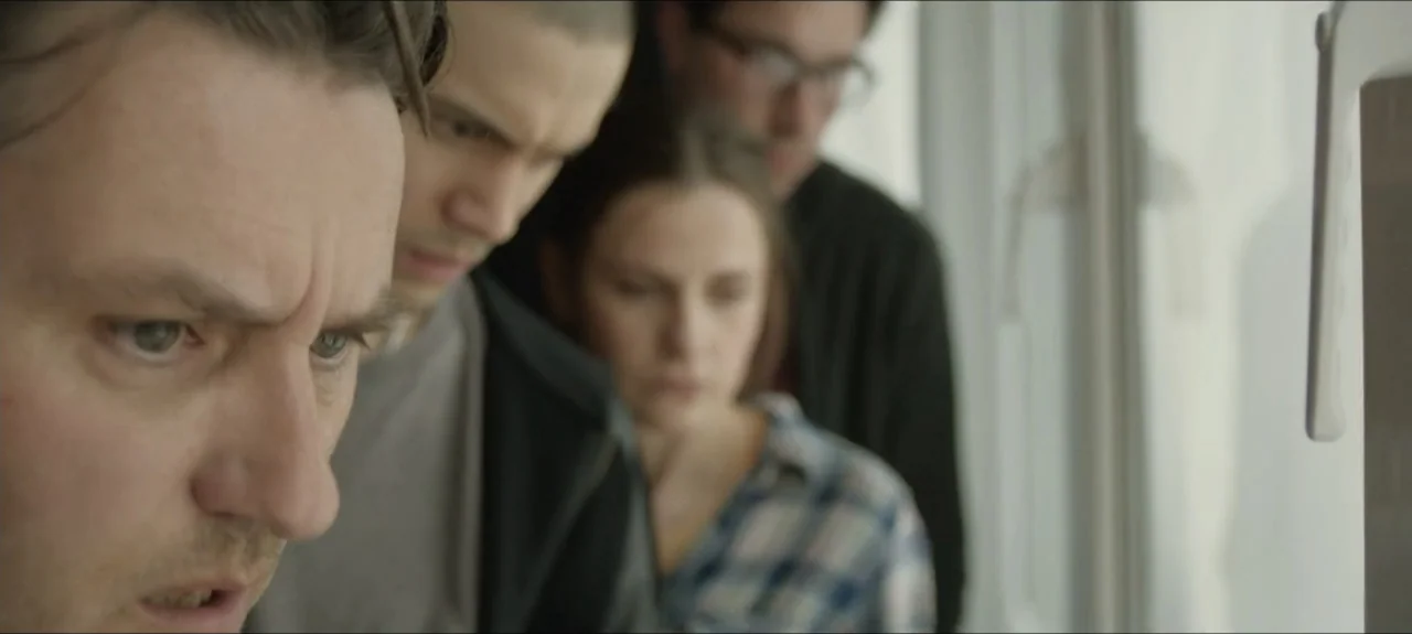 Containment (2015) movie still: medium — Four people are standing in a bright room positioned near a large window. They are standing in a row…