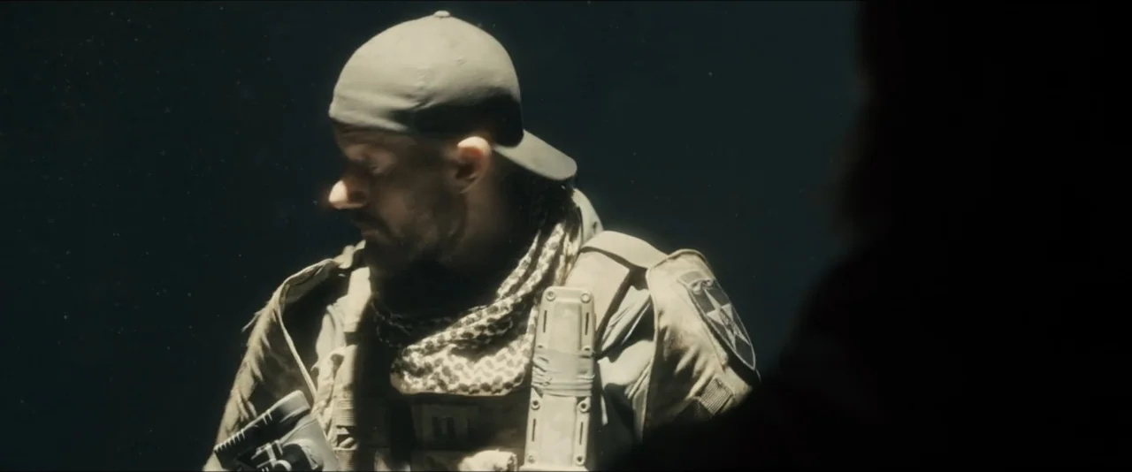 World War Z (2013) movie still: medium — A dark, dimly lit space serves as the backdrop for a tactical operative. A bearded man in tactical gear…