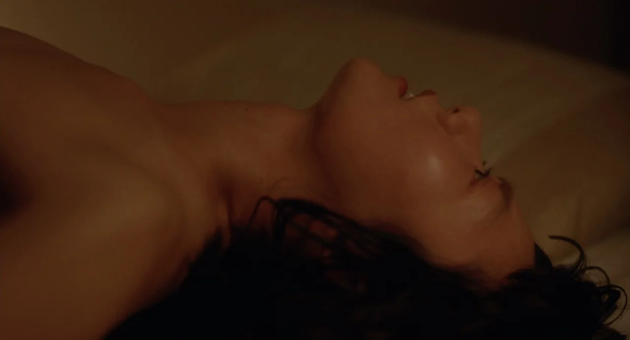 Air Doll (2009) movie still: closeup — A person lies on a soft surface in a darkened interior environment. Their head rests back as they face the…