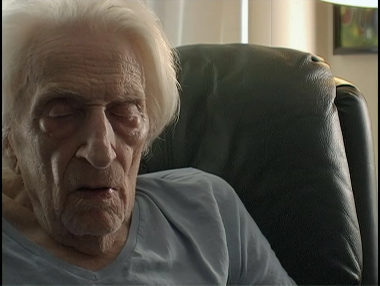 First Cousin Once Removed (2012) movie still: closeup — An elderly man rests in a dark leather chair inside a home. The man has closed eyes and…