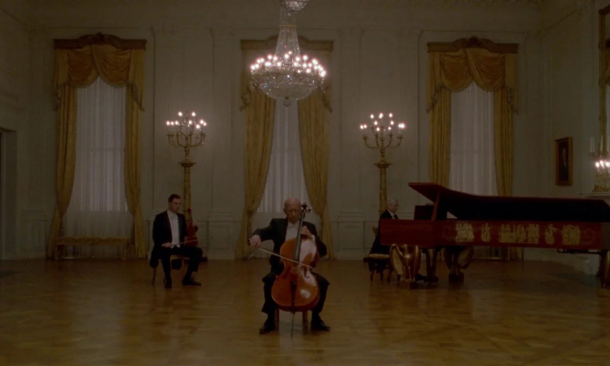 Jackie (2016) movie still: wide — A spacious, neoclassical ballroom features high ceilings, parquet floors, and ornate yellow draped windows. Three…