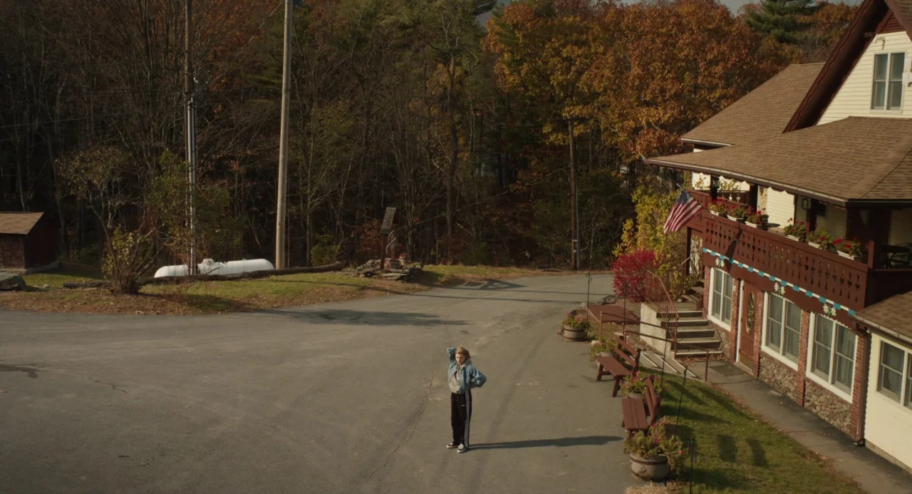 The Miseducation of Cameron Post (2018) movie still: wide — An asphalt driveway leads past a timber-framed inn building with autumn foliage nearby.…