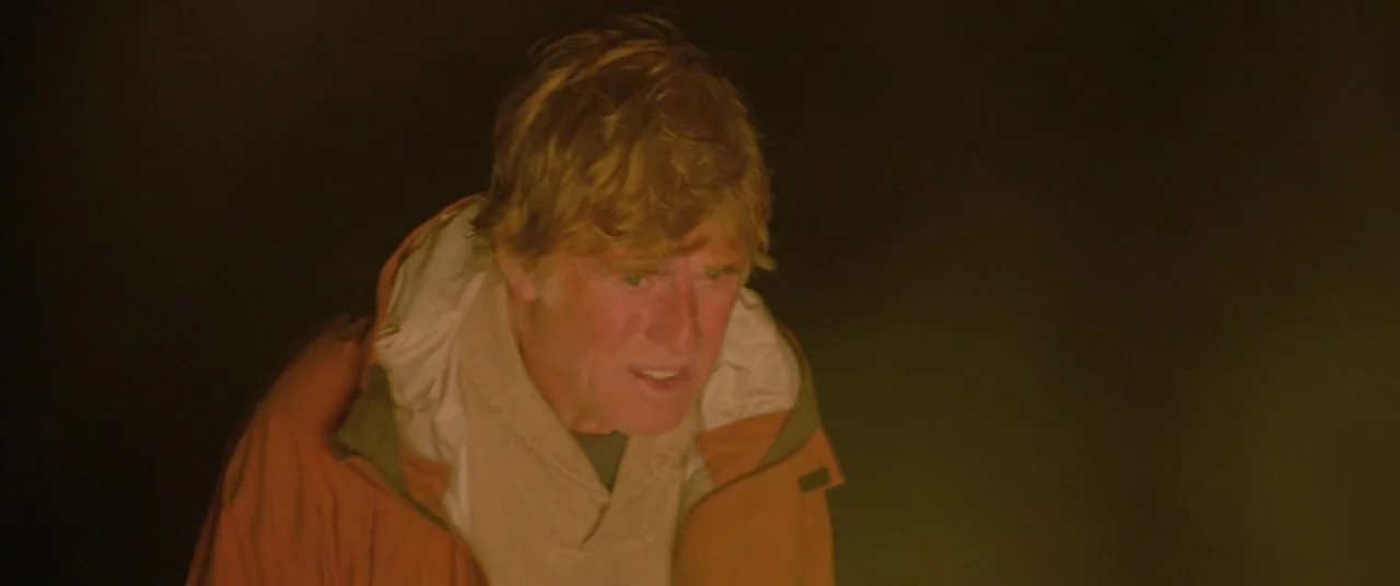 All Is Lost (2013) movie still: closeup — An older man stands in the darkness of a campsite at night. He stares down into the warm, flickering glow…