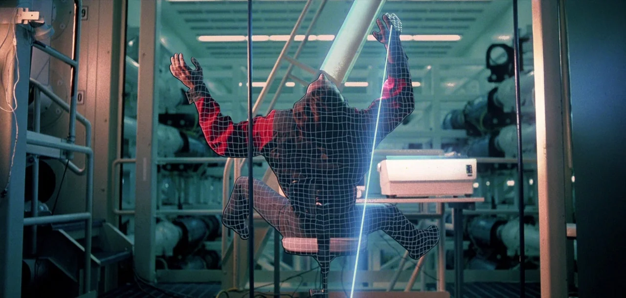 Tron (1982) movie still: medium — A sterile industrial room contains rows of metallic cabinets and a white printer console. A glowing wireframe…