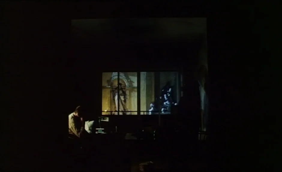 Simon, The Magician (1999) movie still: wide — A darkened interior room is defined by a large bright projection on the wall. A solitary man sits at…
