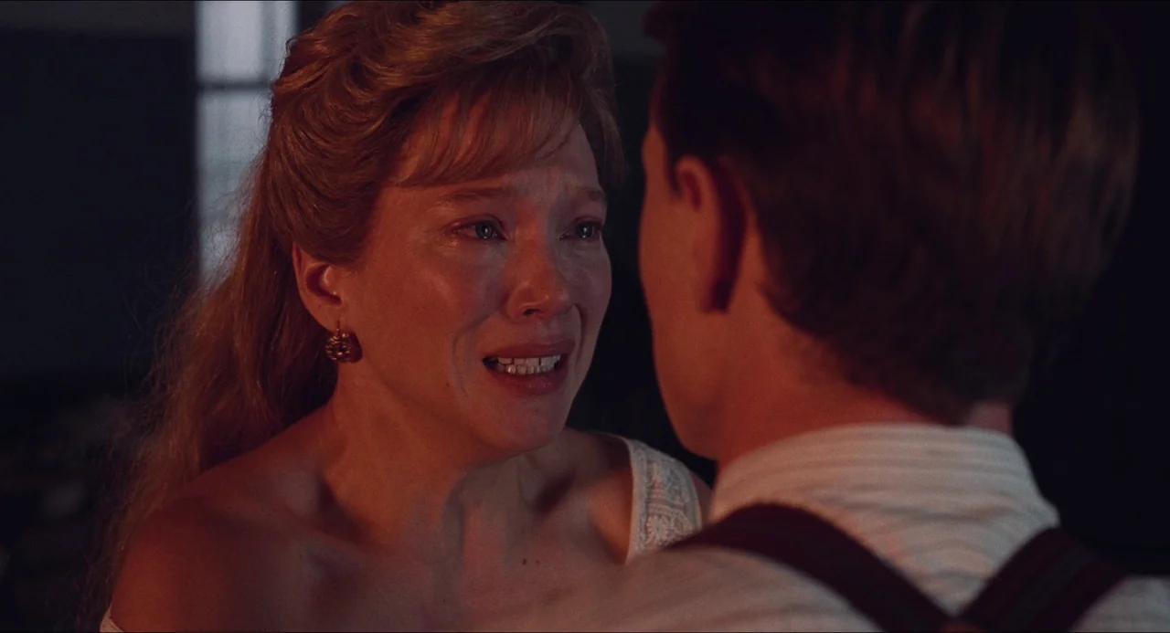 Transformers: Rise of the Beasts (2023) movie still: closeup — A dimly lit interior space with a warm, reddish firelight glow. A woman with tearful…