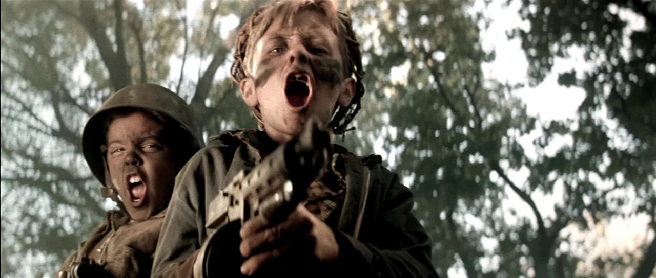 Born On The Fourth of July (1989) movie still: medium — Two young boys play in a dense woodland area with military-themed props. They shout…