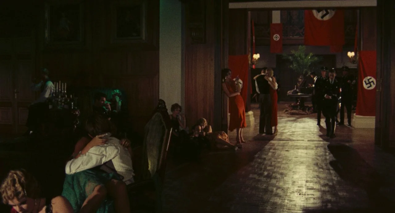 The Damned (1969) movie still: wide — An opulent wood-paneled ballroom is adorned with large red banners bearing white swastika symbols. Multiple…