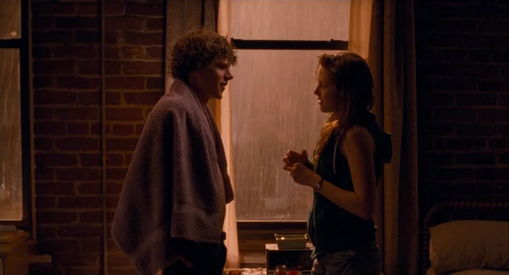 Adventureland (2009) movie still: medium — An interior apartment with exposed brick walls is dark and dimly lit. A man with a towel and a woman in a…