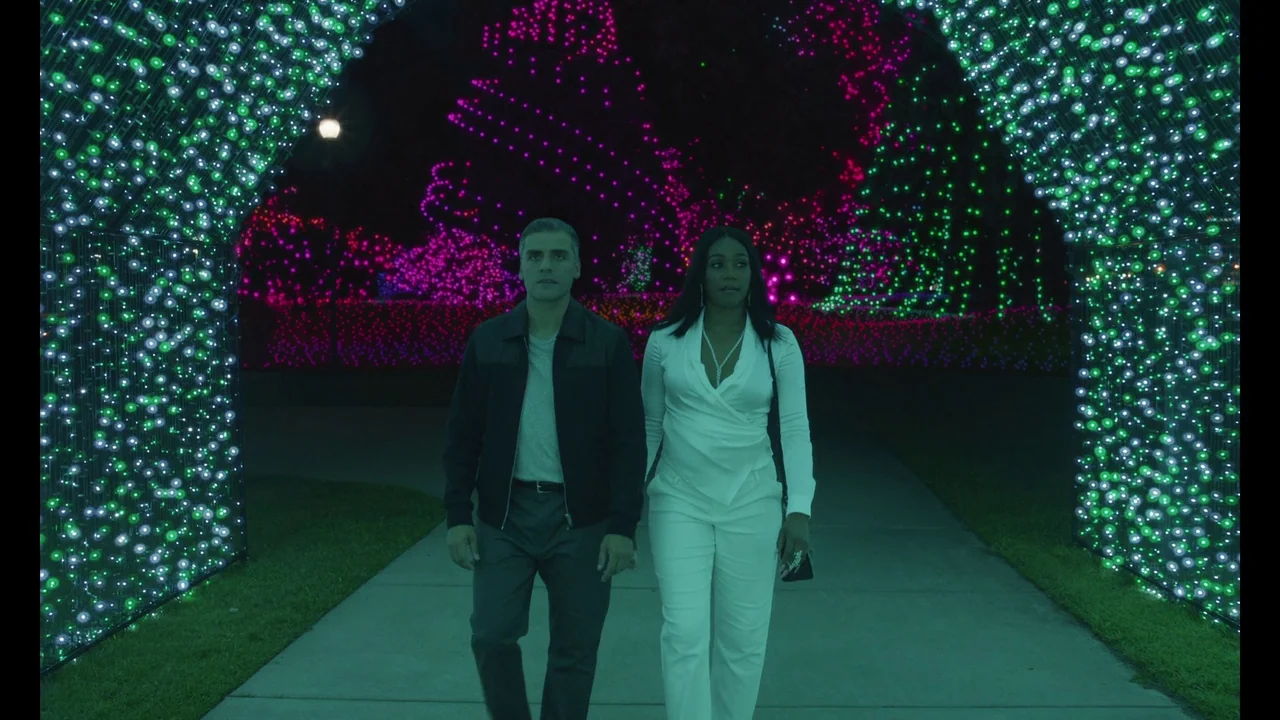 The Card Counter (2021) movie still: fullbody — Two individuals walk through an arched pathway lined with thousands of glowing green lights. Behind…