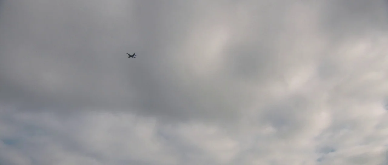 Joe (2013) movie still: establishing — A vast expanse of gray overcast sky fills the frame. A small airplane is flying through the center of the…
