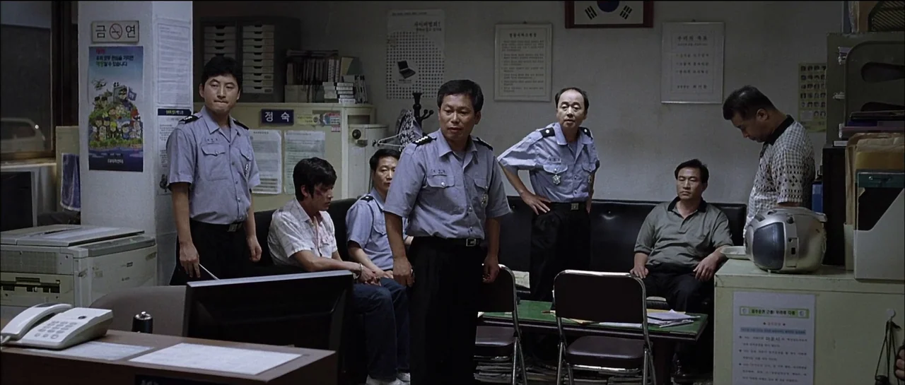 The Chaser (2008) movie still: wide — A cluttered administrative room filled with posters, filing cabinets, and standard Korean office equipment.…