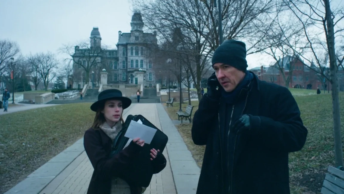 Adult World (2013) movie still: medium — A stone institutional building sits in the background of a paved campus walkway. A woman presents papers to…