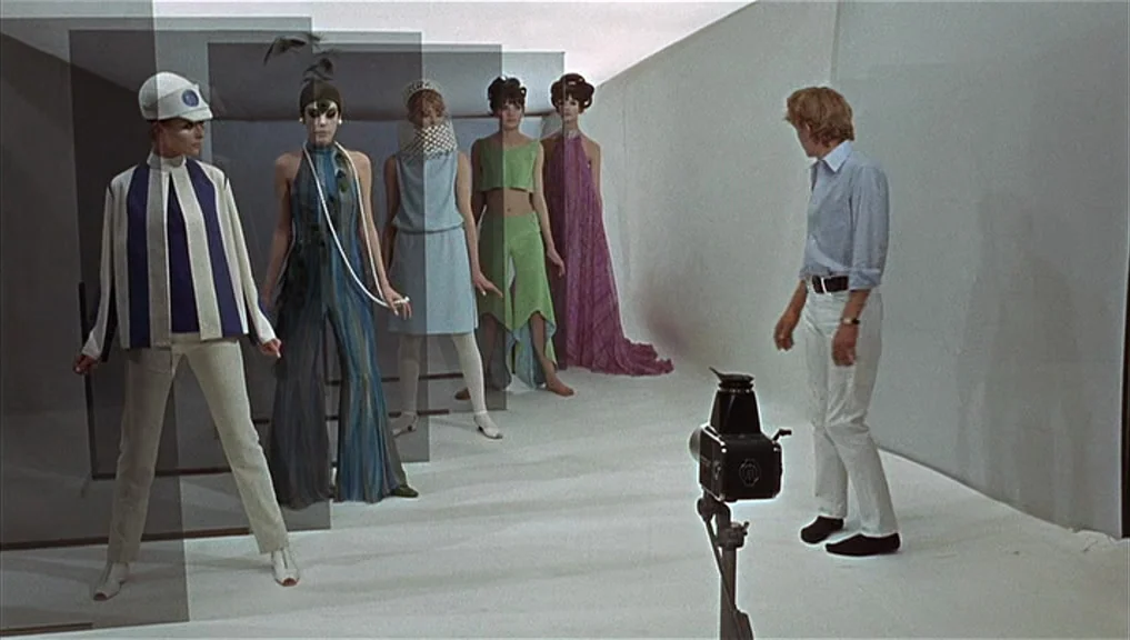 Blow-Up (1966) movie still: fullbody — A stark white photography studio features a series of translucent dark panels in rows. Five female models…