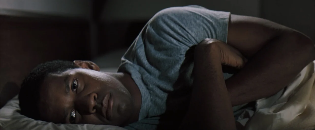 The Pelican Brief (1993) movie still: closeup — A dimly lit room at night features a person lying in a bed. The man rests on his side with his hands…