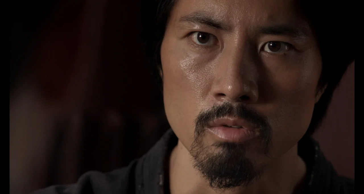 Ninja: Shadow of a Tear (2013) movie still: closeup — A close portrait of a man in an dimly lit interior environment. The subject looks directly…