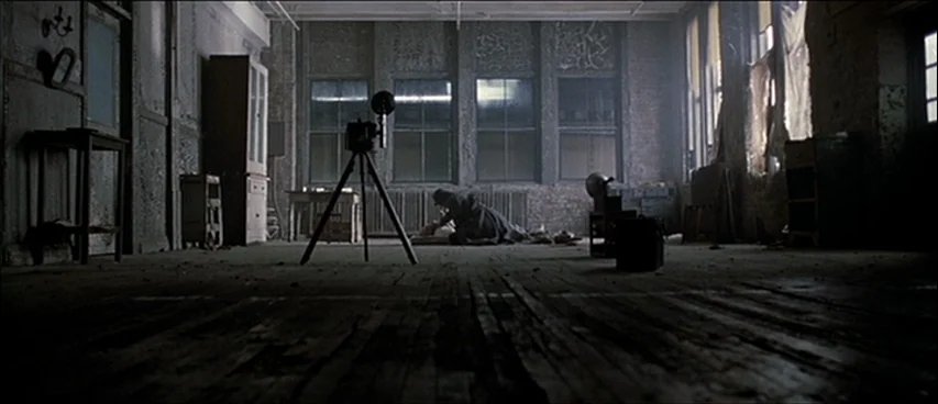 Road To Perdition (2002) movie still: wide — A spacious, weathered room with worn wooden floorboards and tall grid-paned windows. A man in a long…