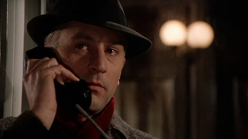 Once Upon A Time In America (1984) movie still: closeup — A man stands inside a dimly lit structure at night. He holds a black telephone handset to…