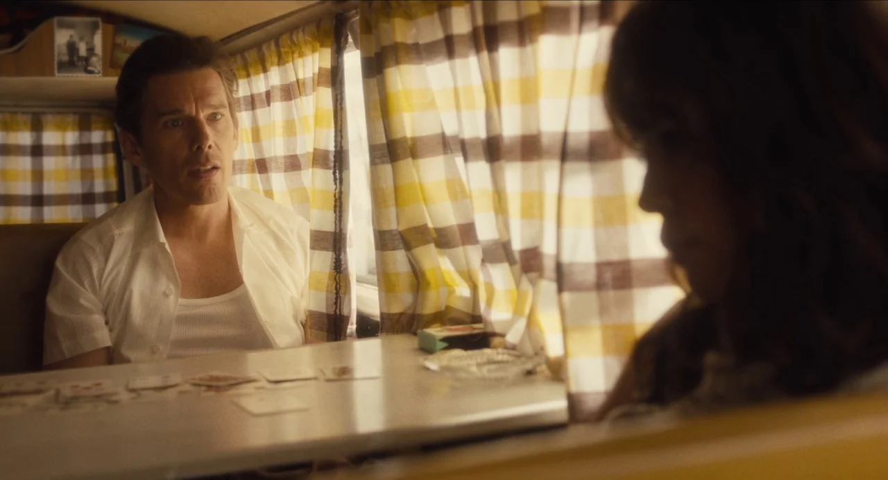 Born To Be Blue (2015) movie still: medium — Inside a small campervan with plaid curtains covering the windows during the day. A man is seated at a…