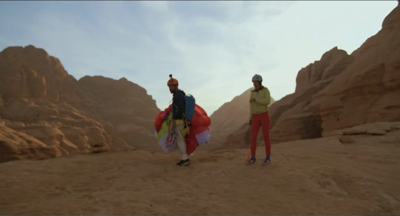 Crooked Trees Gon Give Me Wings (2022) movie still: fullbody — A flat rocky plateau is surrounded by large tan sandstone cliffs and mountains. Two…