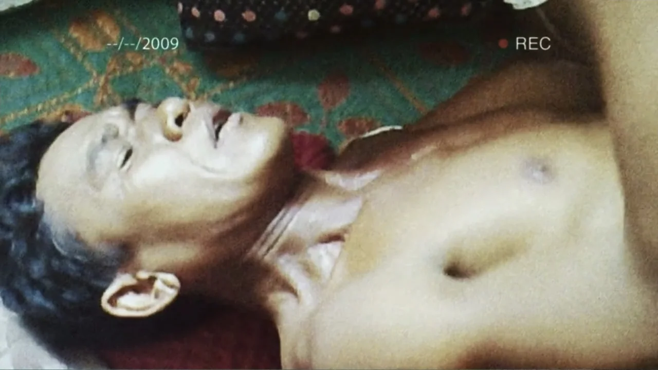 A Cambodian Spring (2018) movie still: closeup — A close view of a person lying on a patterned carpeted floor. A shirtless man is resting his head…