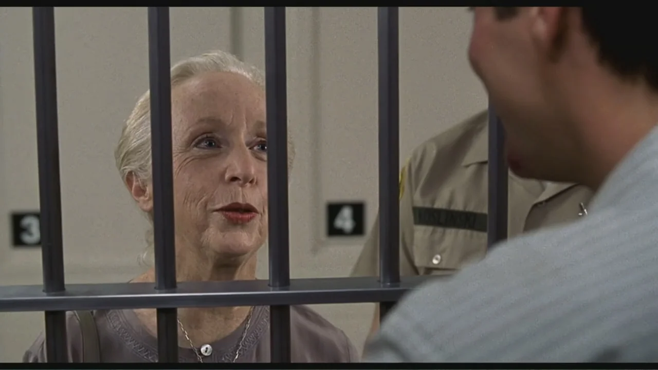 Liar Liar (1997) movie still: medium — A sterile visitation room has light grey walls with numbered black signs. An elderly woman stands behind…