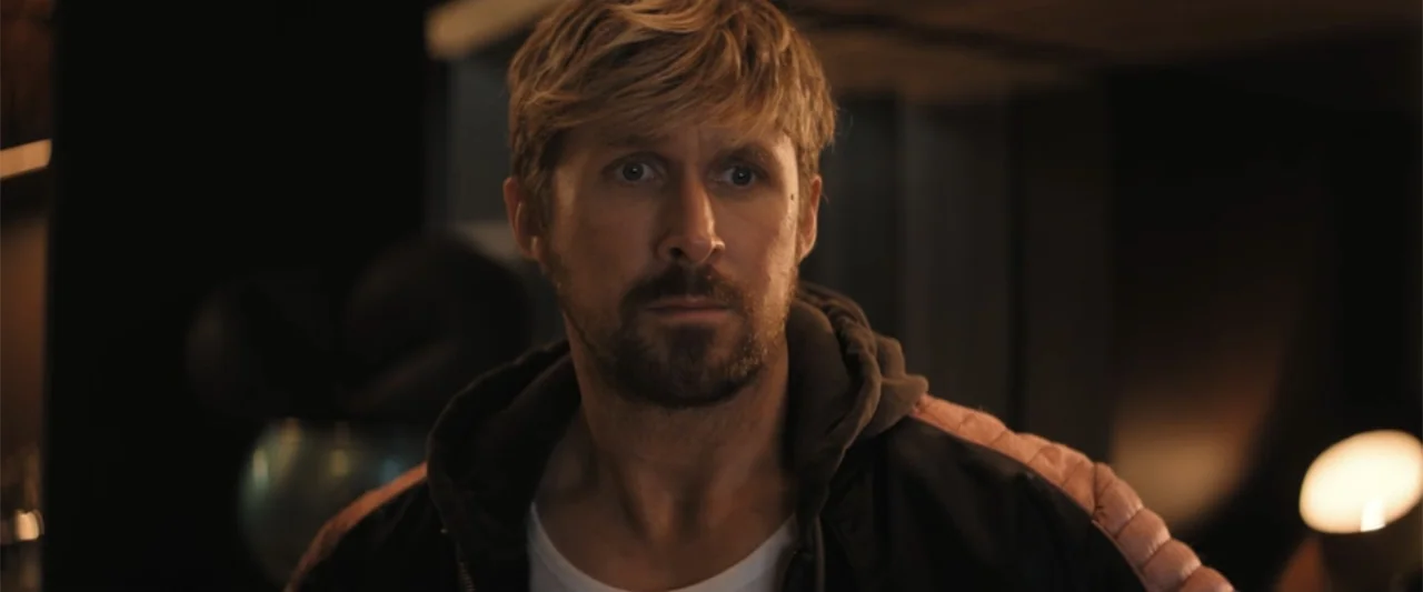 The Fall Guy (2024) movie still: medium — A dimly lit contemporary space features dark walls and soft ambient practical lighting. A man with blonde…