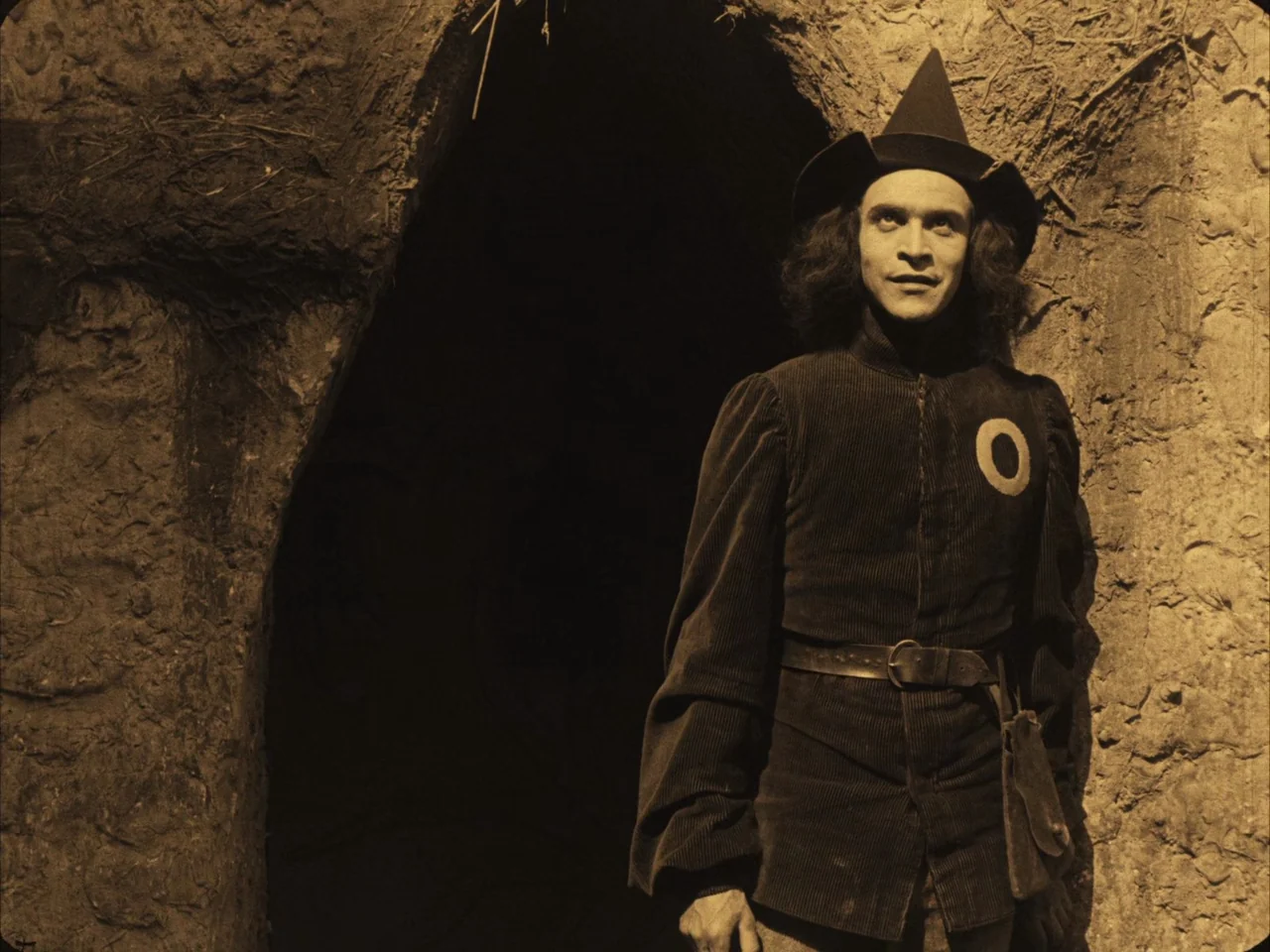 The Golem (1920) movie still: medium — A man stands before a deep, shadowed recess in a rough stone wall. The subject wears a dark medieval-style…