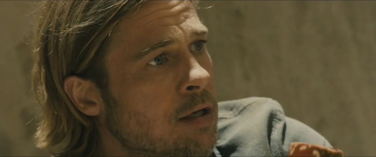 World War Z (2013) movie still: closeup — A man stands inside a room with plain, beige textured walls. He is looking at an unseen person with his…