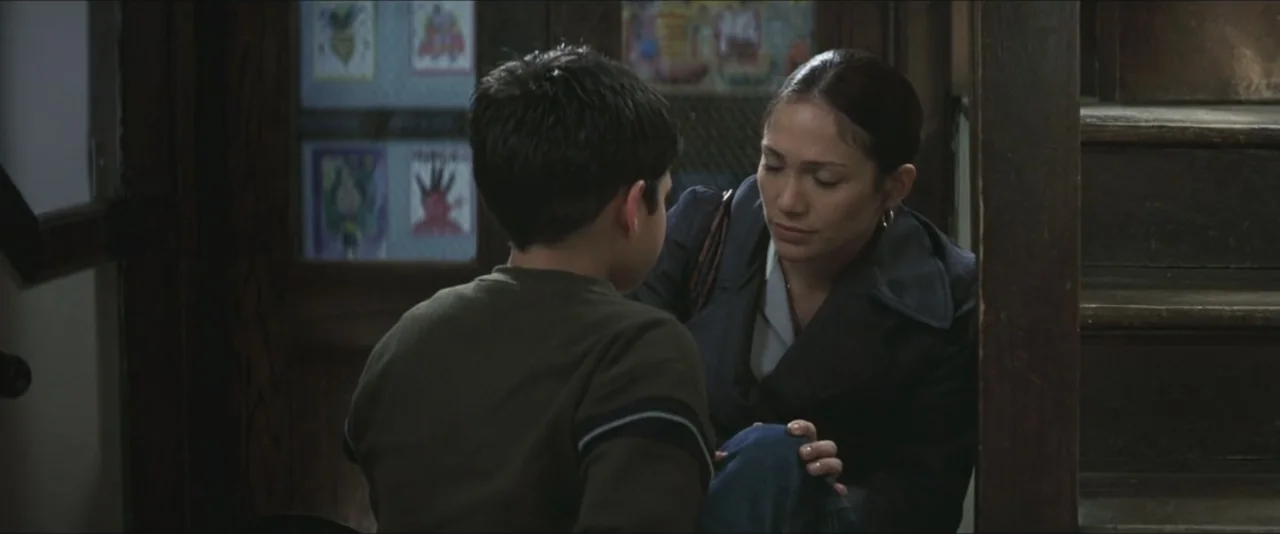 Maid in Manhattan (2002) movie still: medium — A dark wooden stairwell features a doorway with children's drawings taped to the glass. A woman…