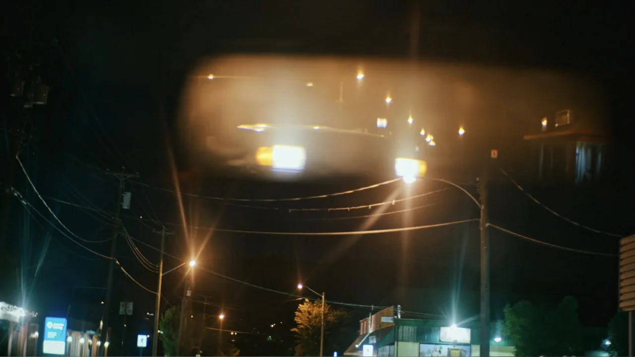 Bullet Proof (2022) movie still: establishing — A dark night scene shows a city street with overhead power lines and lamps. Bright blurry lights are…