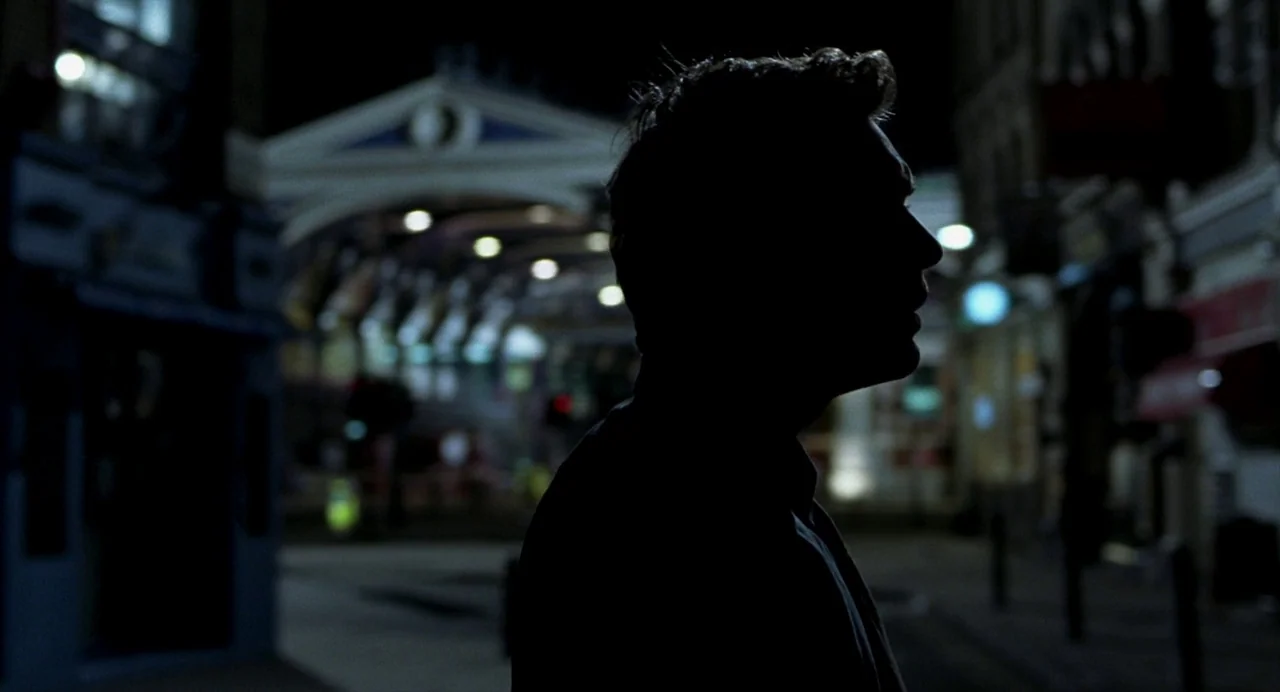 Closer (2004) movie still: medium — A man stands in silhouette against the blurry background of an empty outdoor plaza. The architecture in the…
