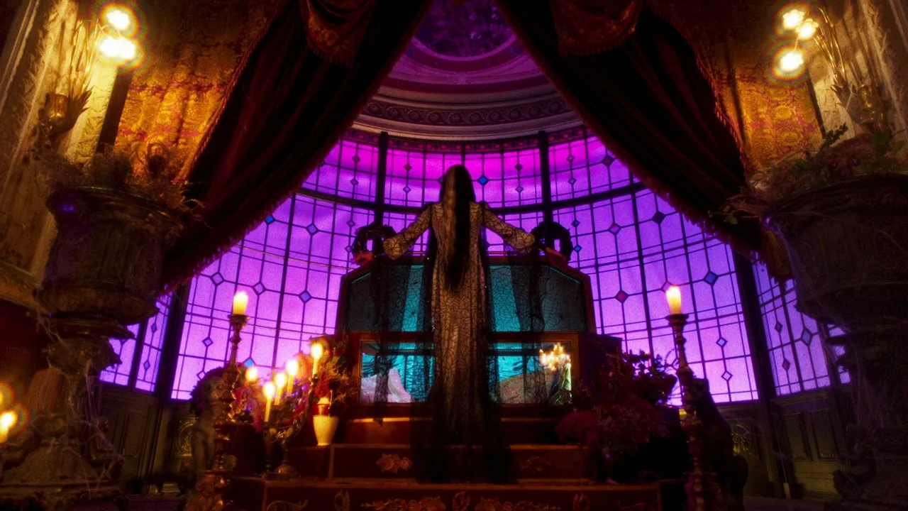 The Munsters (2022) movie still: fullbody — A dark, ornate chamber features a massive stained glass window illuminated in deep violet. A woman in a…