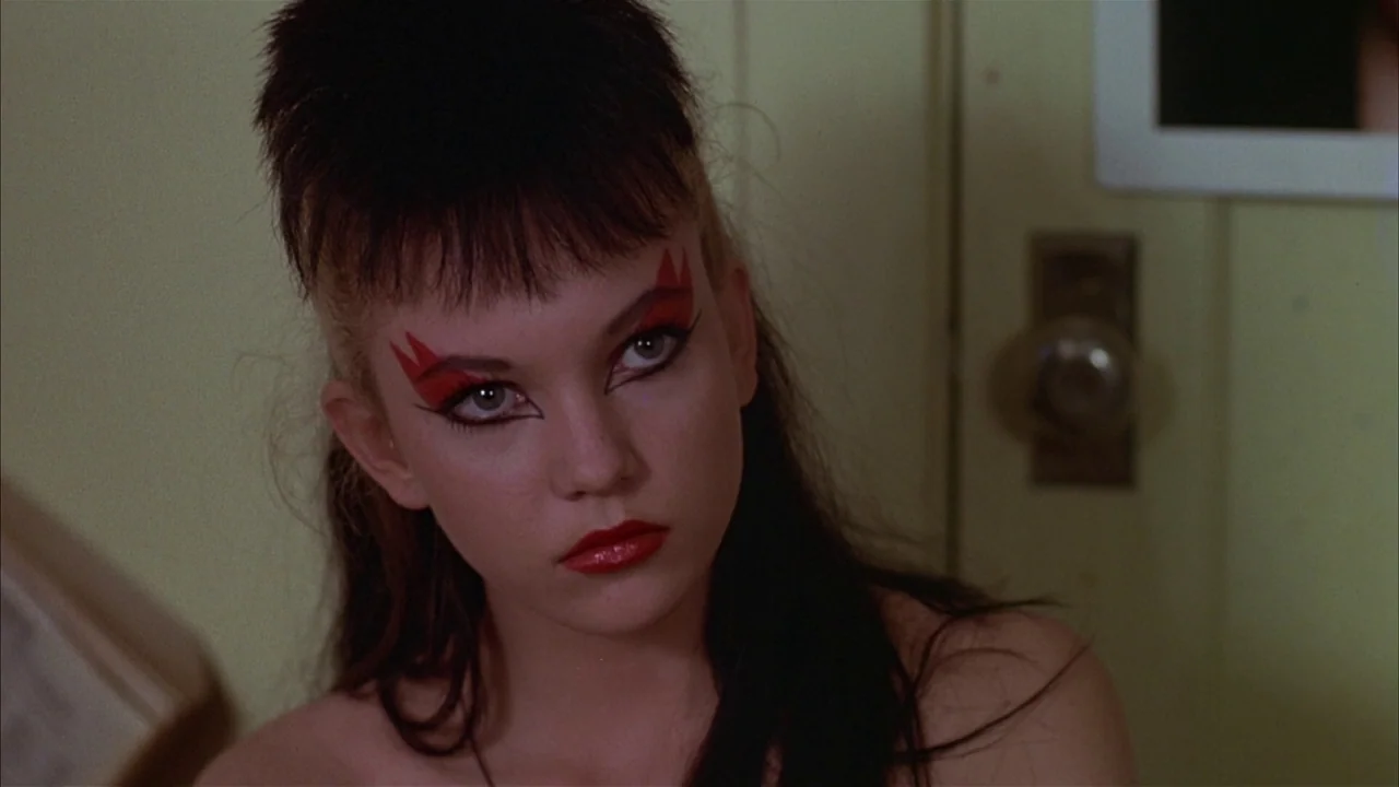 Ladies and Gentlemen, the Fabulous Stains (1985) movie still: closeup — A teenage girl with stylized hair and makeup sits in a sparsely decorated…