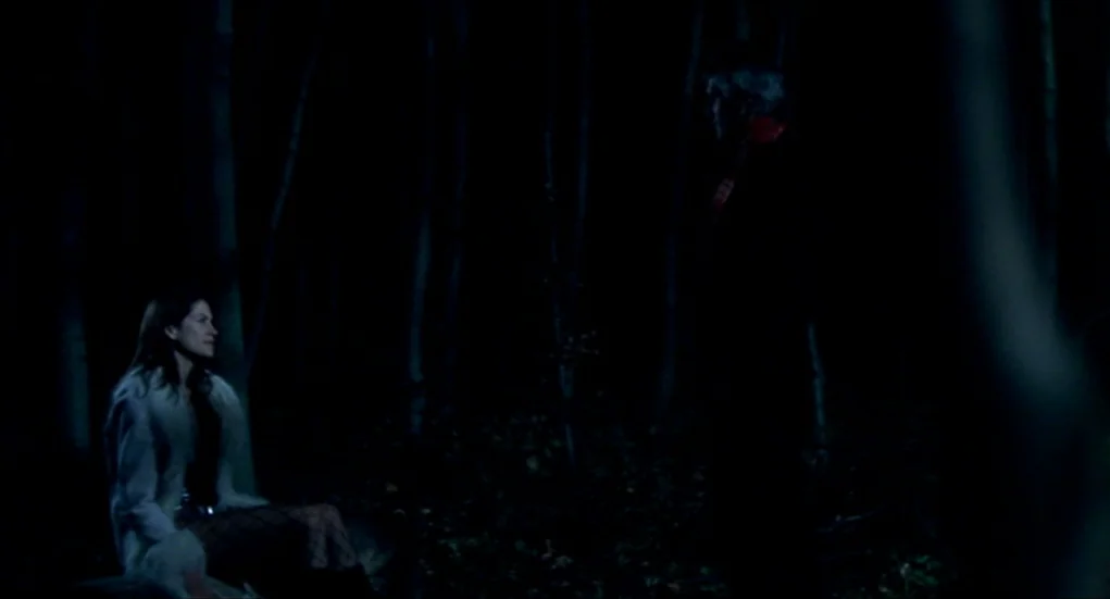 Tiresia (2003) movie still: medium — A dark, dense forest environment at night with tall trees visible in the background. A woman sits on a fallen…