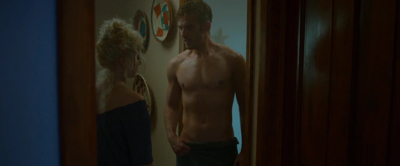 The Guest (2014) movie still: medium — A residential hallway features beige walls adorned with circular woven wall hangings. A shirtless man wrapped…