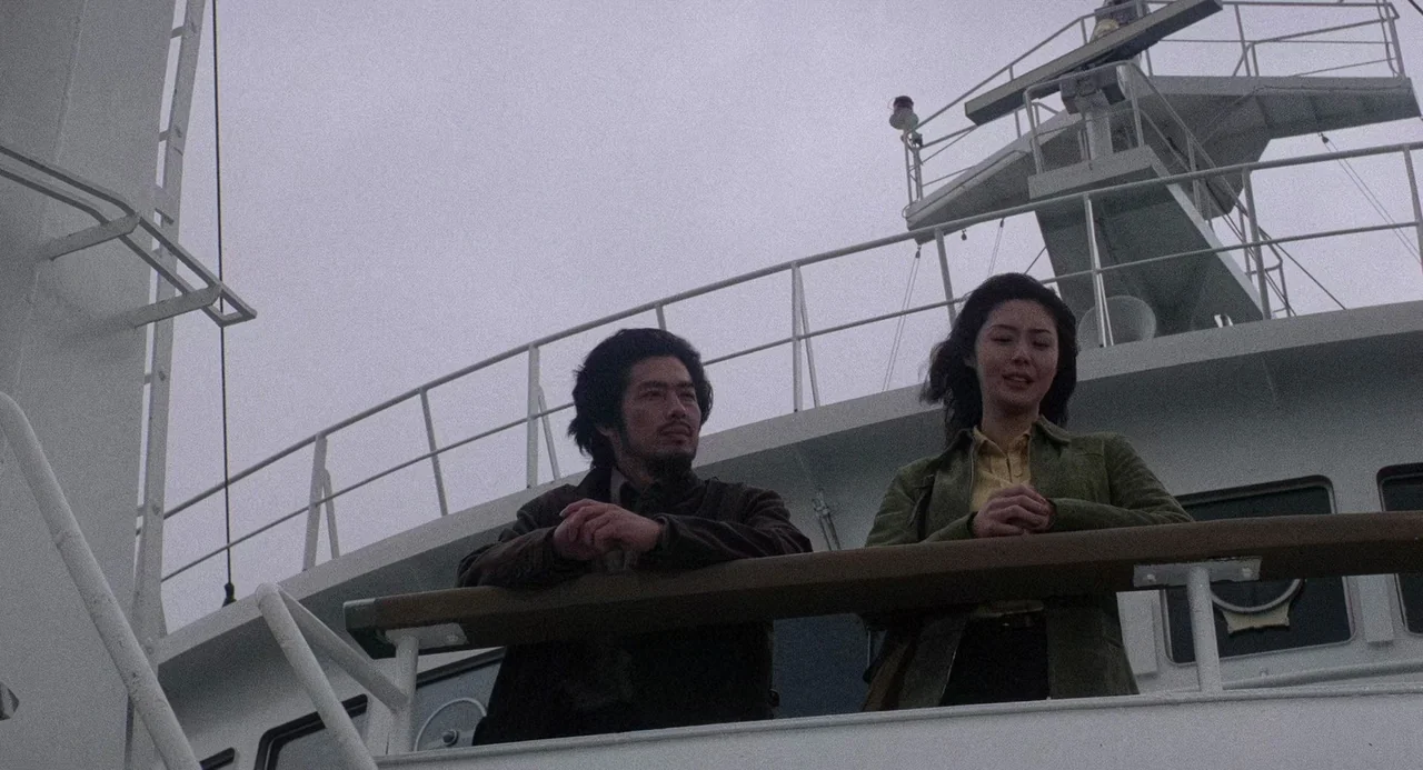 Ringu (1998) movie still: medium — The outdoor deck of a white ship features a metal radar mast overhead. A man and a woman stand together, leaning…