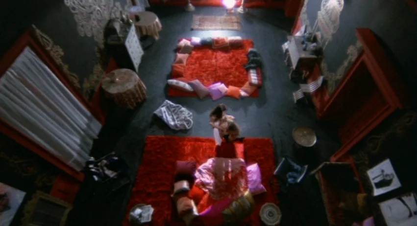 A Lizard In A Woman’s Skin (1971) movie still: wide — A spacious room features two large red carpets covered in piles of scattered cushions. Two…